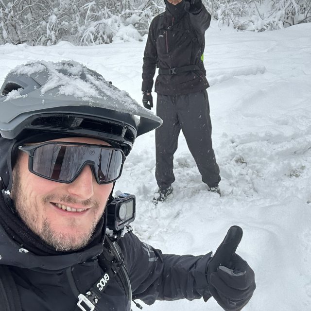 Home Chłopaki na rowerach elektrycznych płyną przez las po dużym śniegu. Ujęcie typu 'flow' podkreśla zabawę i lekkość prowadzenia nowoczesnych rowerów elektrycznych typu trail, które mimo dodatkowej wagi baterii, zachowują niesamowitą zwinność w powietrzu